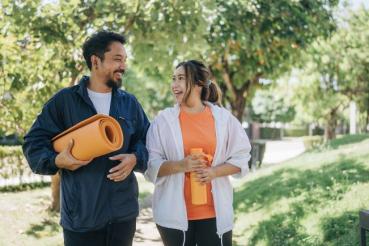 Two people carrying exercise equipment chatting happily in a sunny park.